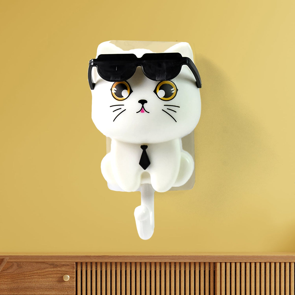 White cat-shaped wall hook with sunglasses and a tie, mounted on a yellow wall above a wooden surface.