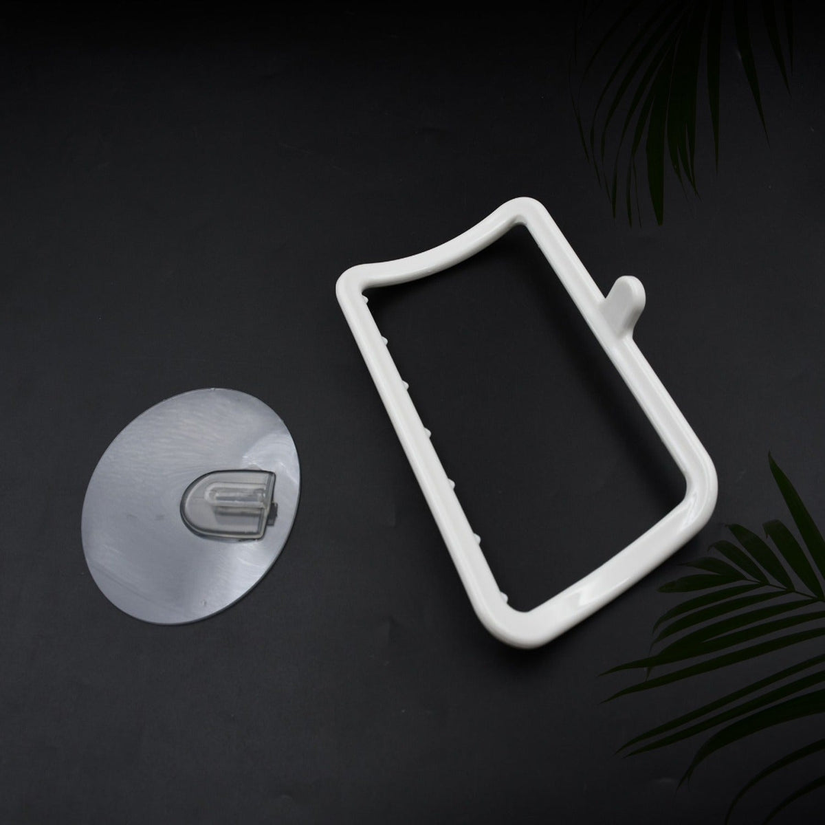 White plastic towel holder and a clear adhesive hook on a dark background with green foliage.