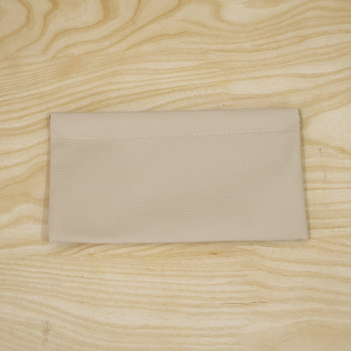 A cream textured faux leather pouch lying flat on a light wooden surface with visible grain.