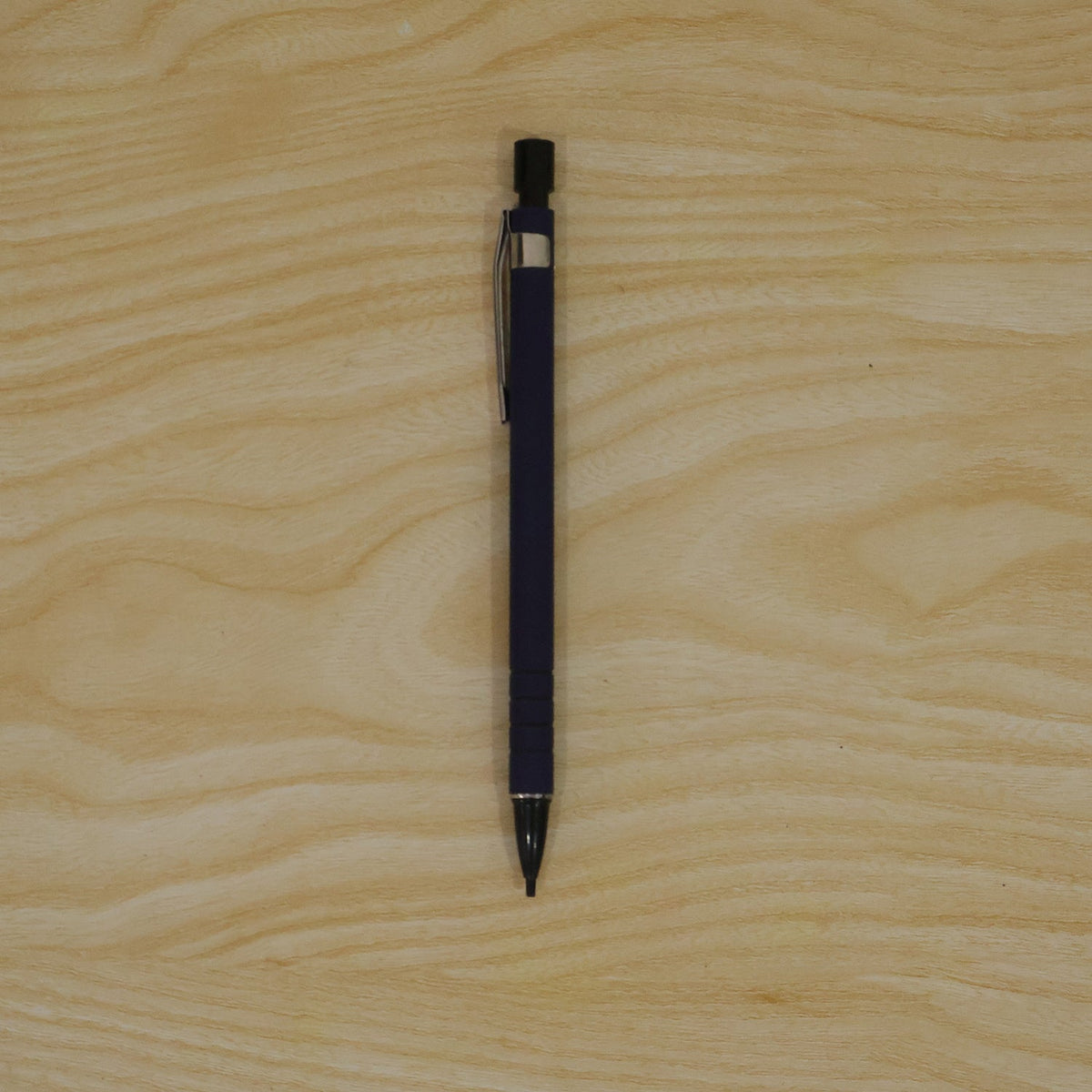 A blue mechanical pencil with a black tip and clip is centered on a light wooden surface.
