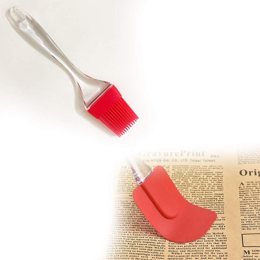 A red silicone brush with a clear handle is shown above a red silicone spatula with a clear handle on a newspaper background.