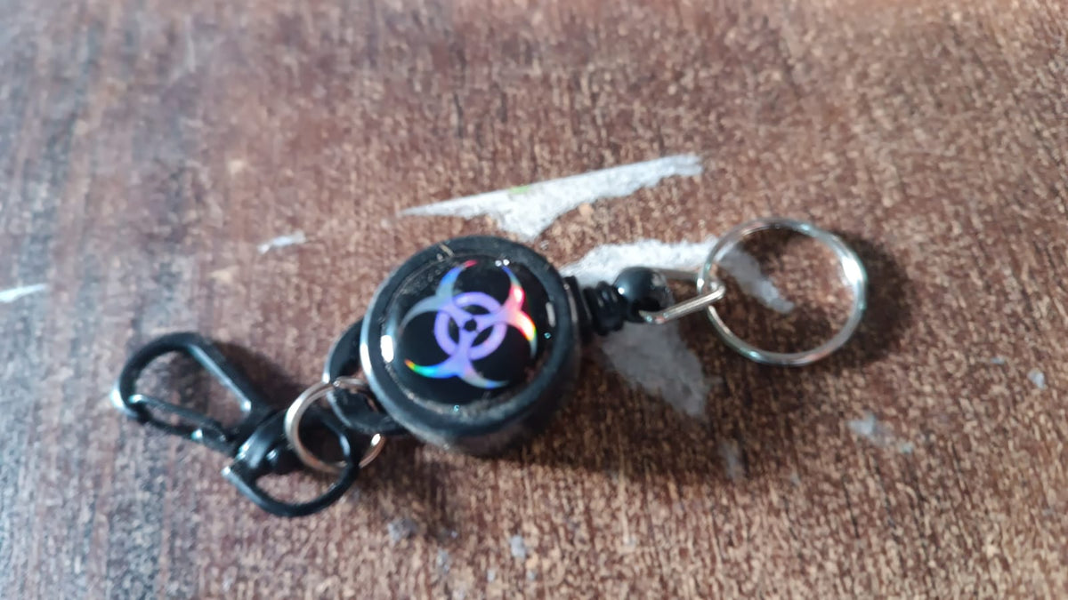 A black retractable keychain with a biohazard symbol resting on a wooden surface.