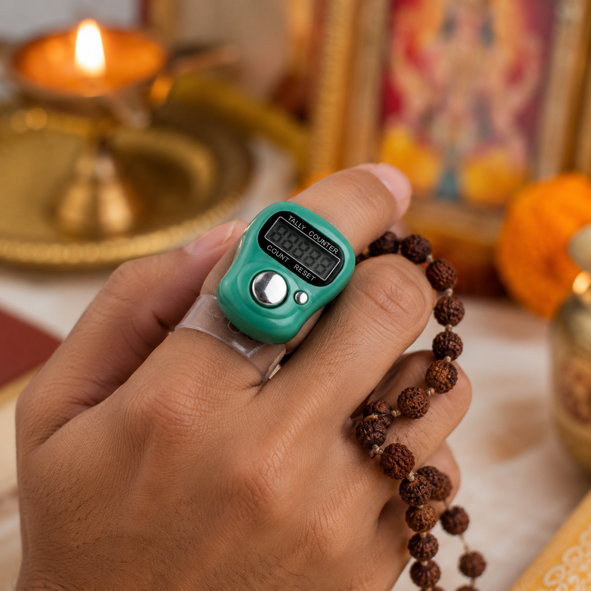 A hand holds a green digital tally counter on a finger, with a string of brown prayer beads. A lit lamp is in the background.