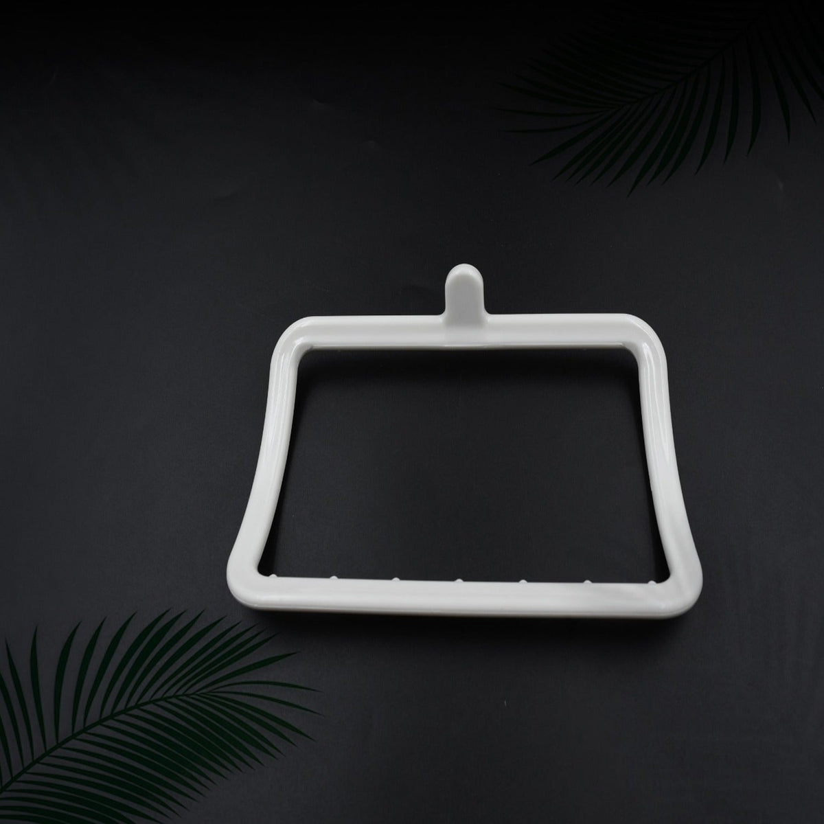 Top-down view of the white plastic towel holder with a textured bottom edge on a dark background with green foliage.