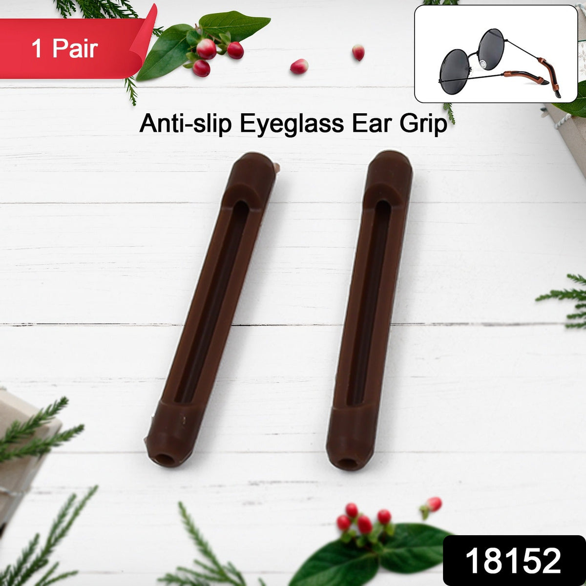 Two brown anti-slip eyeglass ear grips displayed on a white wooden surface with festive green and red decorations.