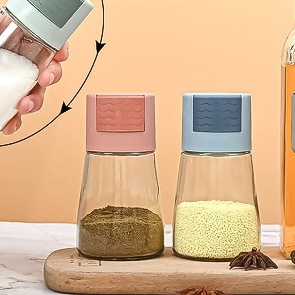 Two glass spice dispensers with pink and blue tops sit on a wooden board, filled with brown and yellow spices.