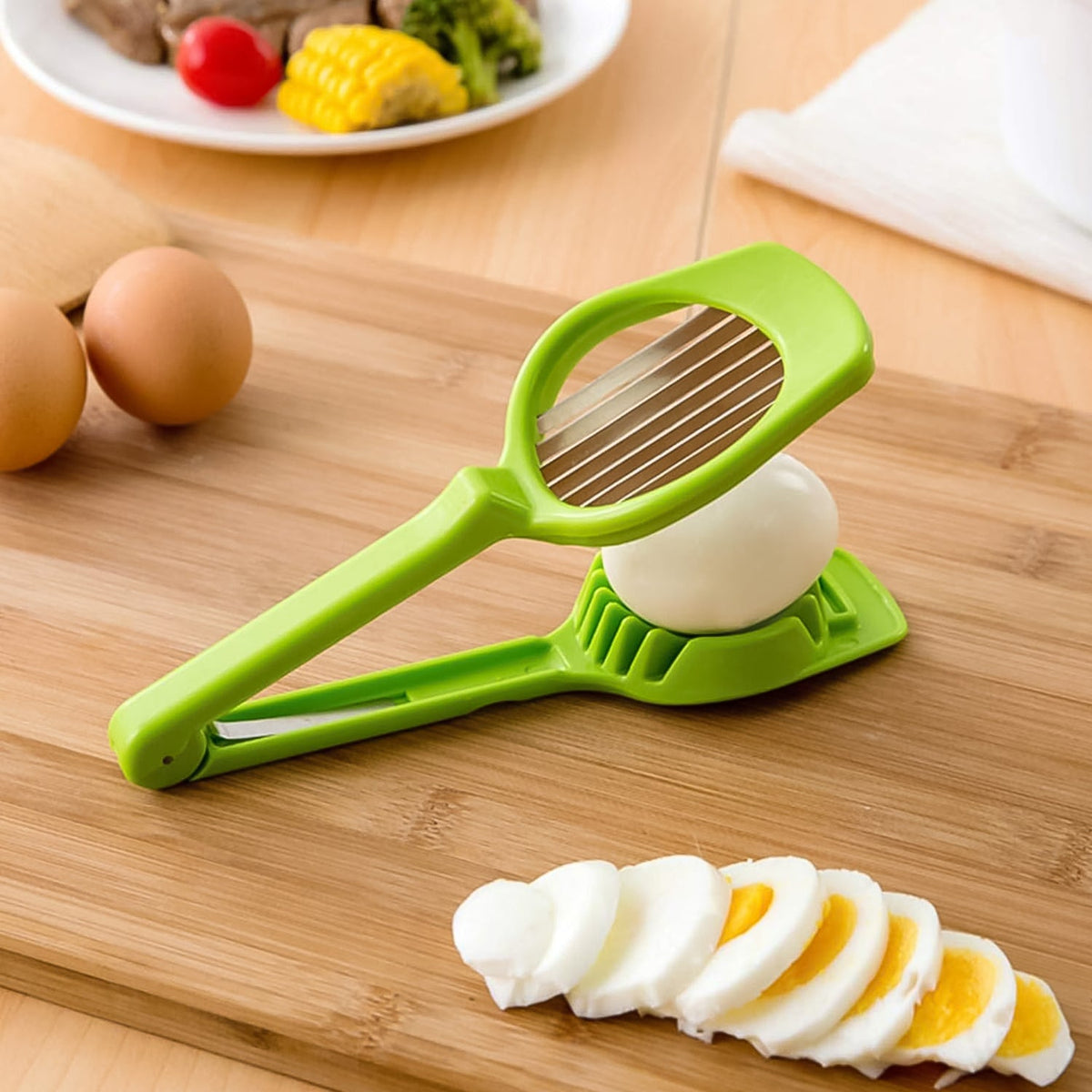 A green plastic slicer with metal blades rests on a wooden board next to a whole egg and perfectly sliced egg pieces.