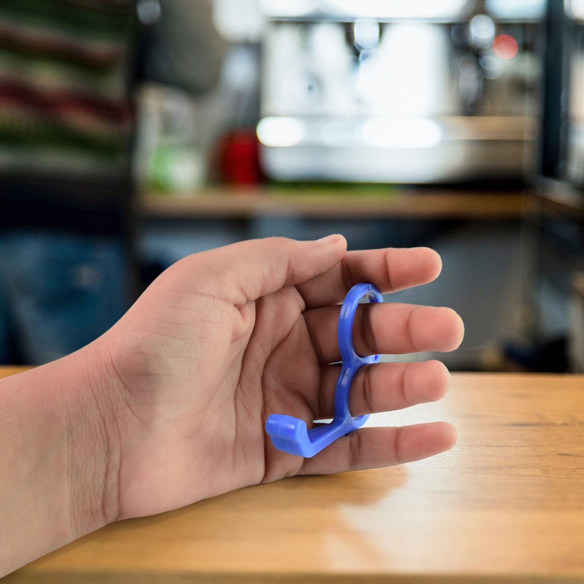 A hand demonstrates holding a blue plastic finger ring phone holder with two fingers.