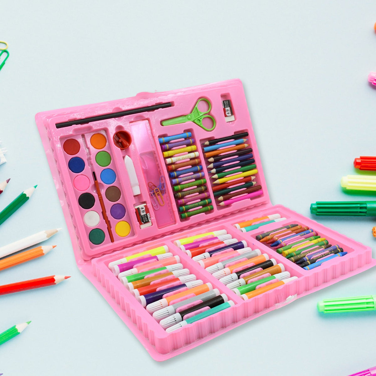 The open pink art kit with its colorful contents is angled on a light blue surface, with loose art supplies scattered nearby.
