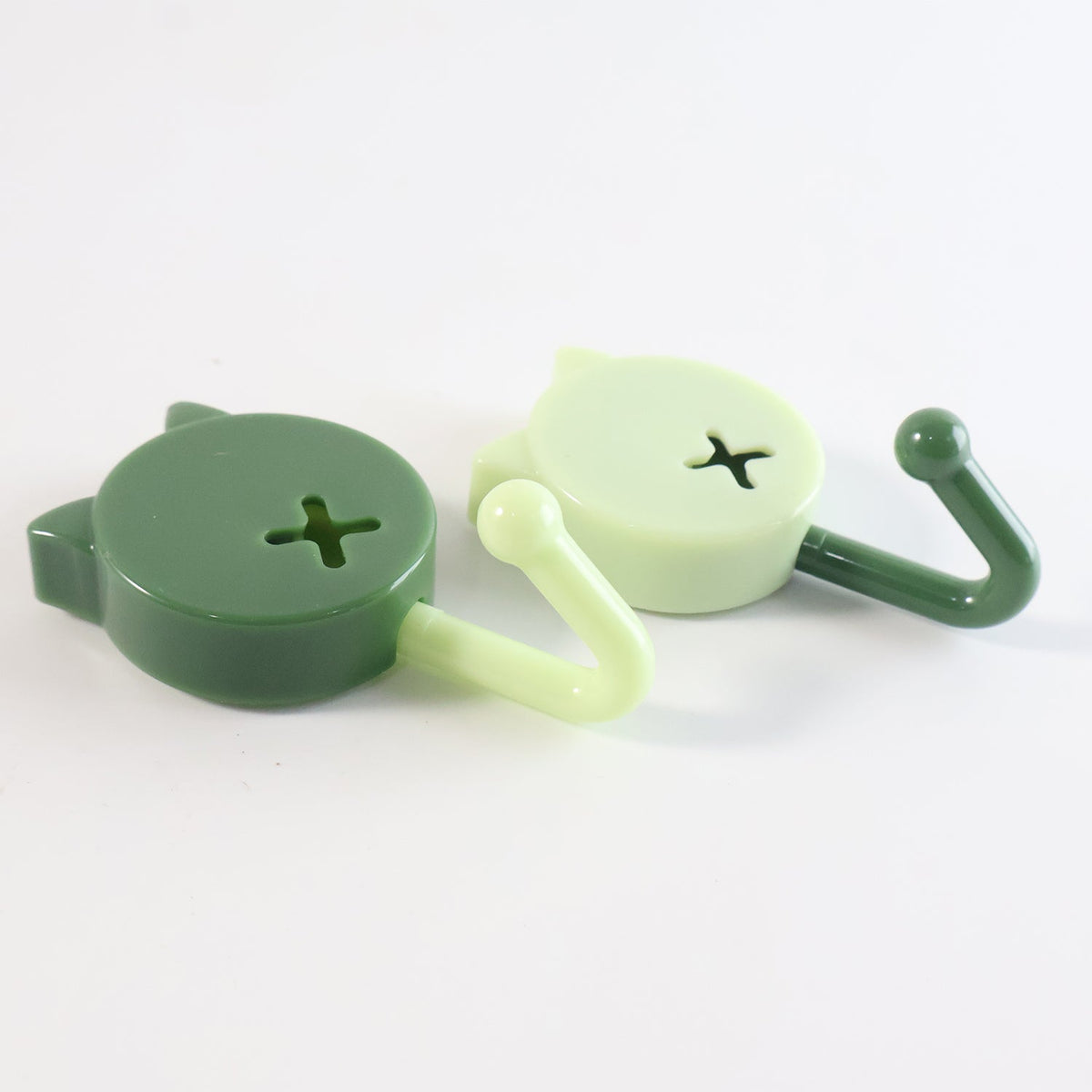 Two cat-shaped wall hooks, one dark green and one light green, lying on a white surface, showing their side profiles.