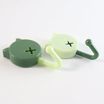 Two cat-shaped wall hooks, one dark green and one light green, lying on a white surface, showing their side profiles.
