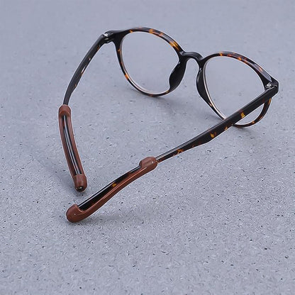 Tortoiseshell eyeglasses with brown anti-slip ear grips on the temples, resting on a gray textured surface.
