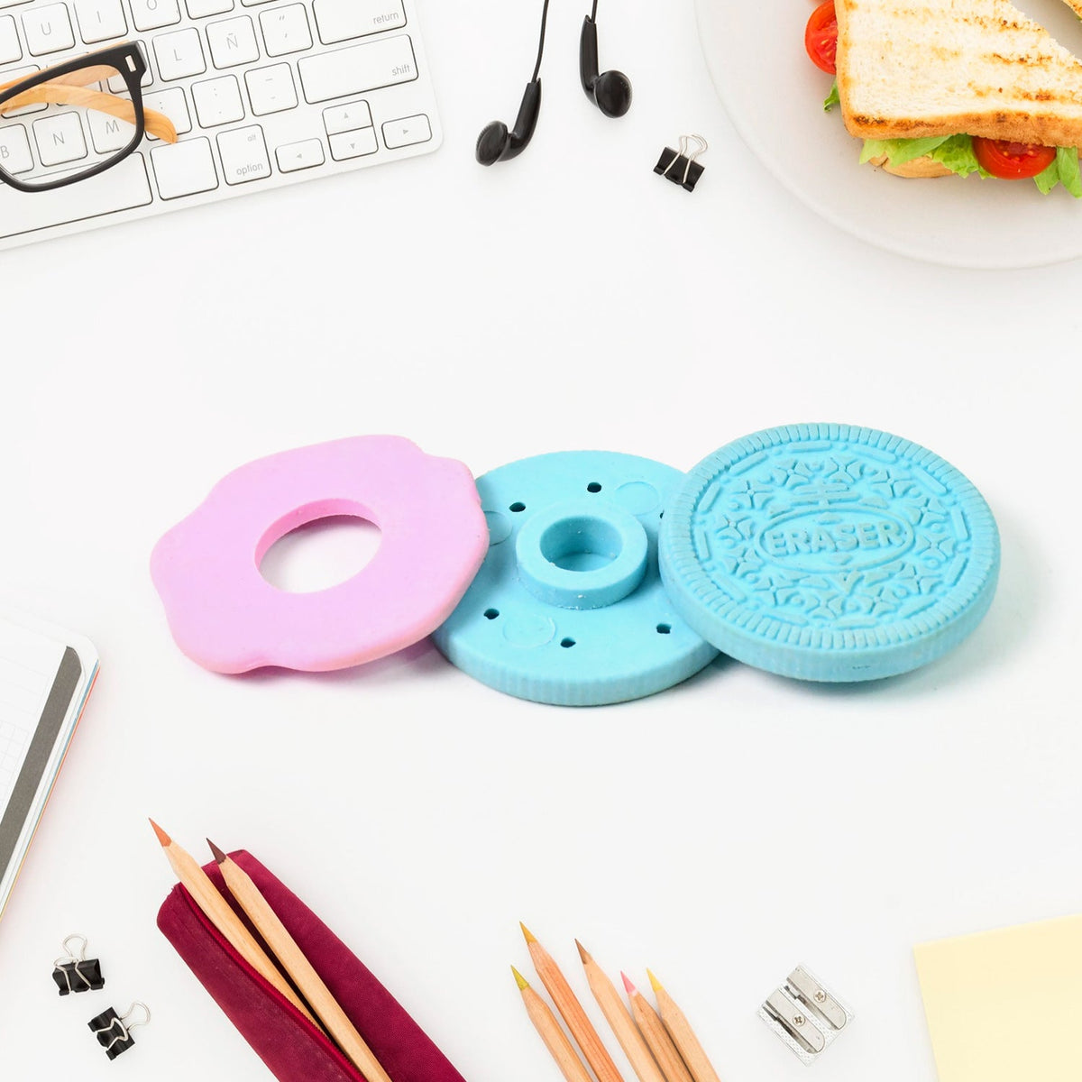 A disassembled blue and pink cookie eraser lays on a white desk with pencils, a sharpener, and other office items.