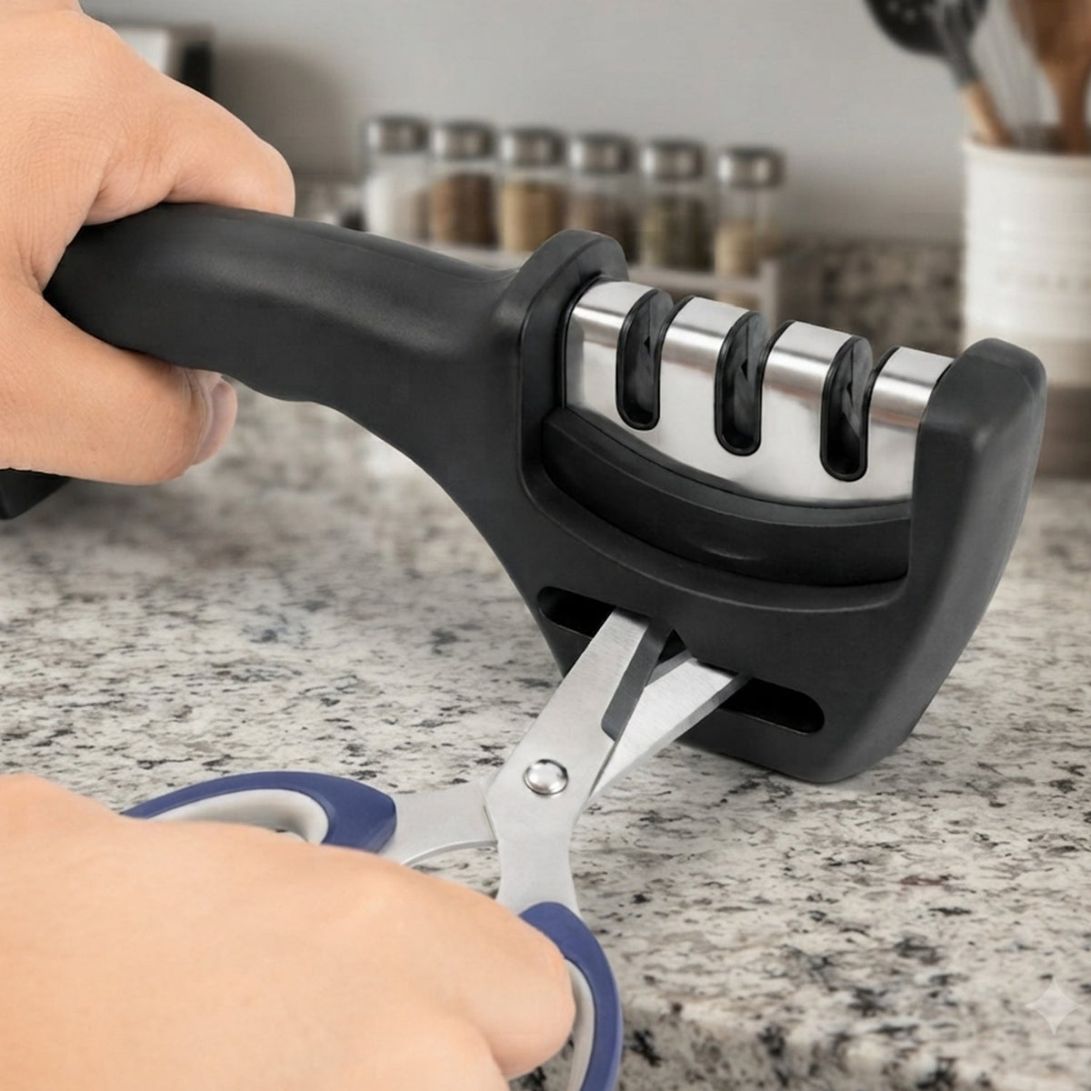 Hands hold a black three-stage sharpener while sharpening blue-handled scissors on a light speckled countertop.