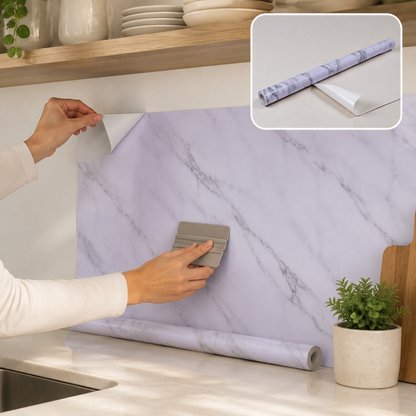 A person applies white and grey marble pattern self-adhesive wallpaper to a kitchen wall above a counter.