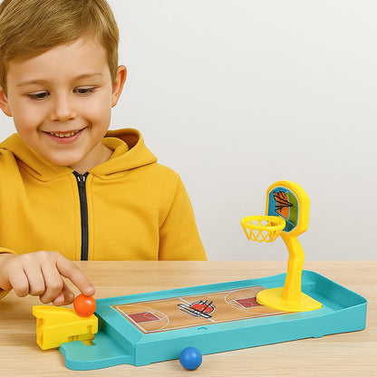A smiling boy in a yellow hoodie plays with the miniature basketball game, pressing the launcher with his finger.
