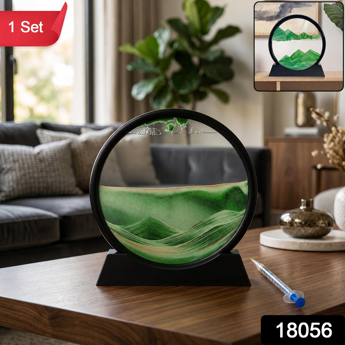 A black-framed circular sand art display with green and gold sand creating a landscape, sitting on a wooden table