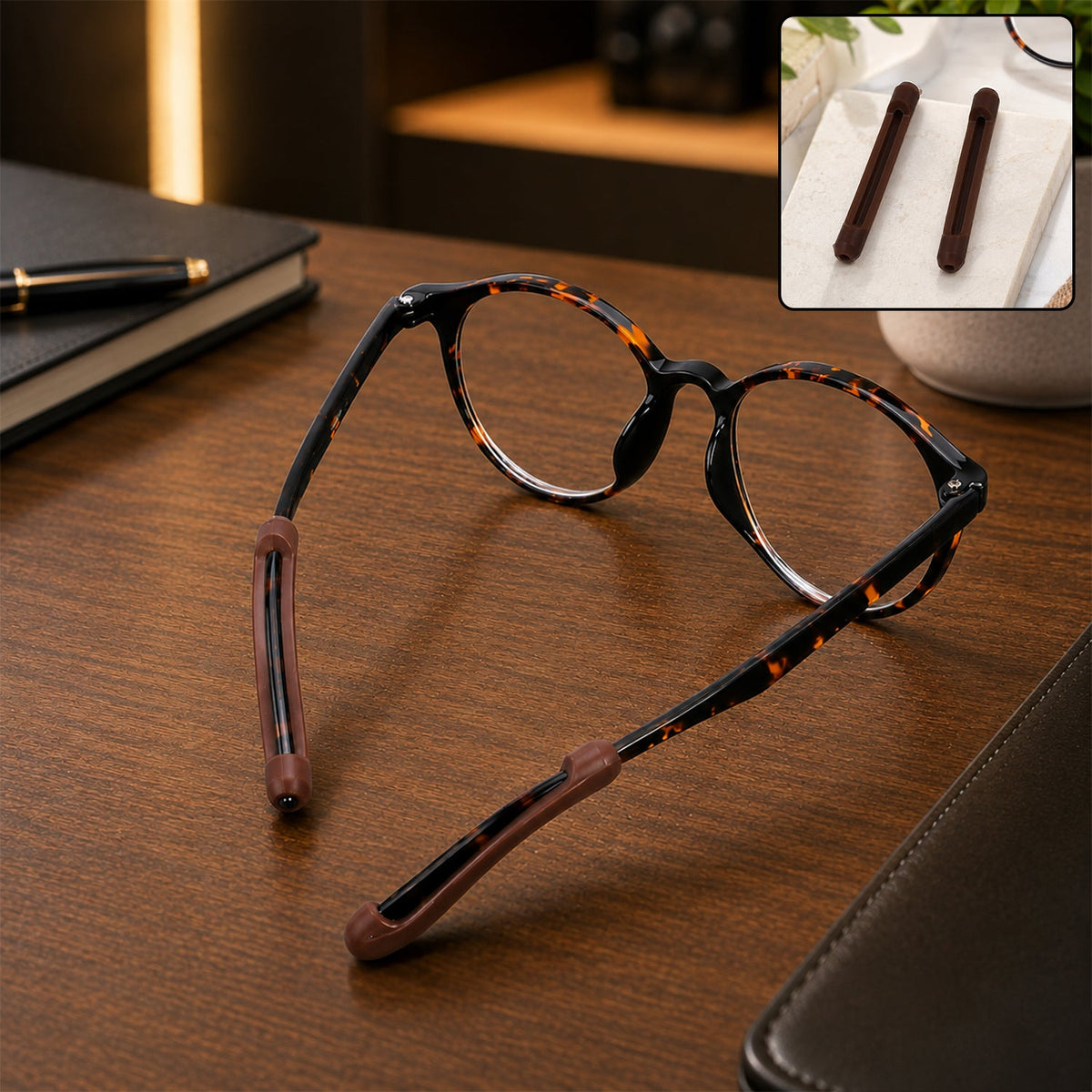 Tortoiseshell eyeglasses with brown anti-slip ear grips on the temples, resting on a wooden desk with a notebook.