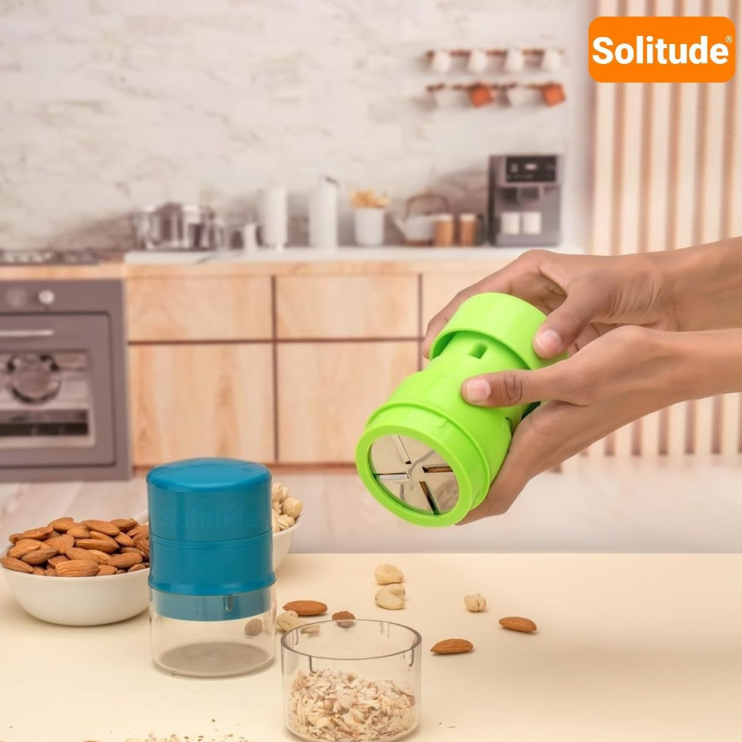Hands hold a green dry fruit slicer over a clear container of sliced nuts, with a blue slicer nearby.