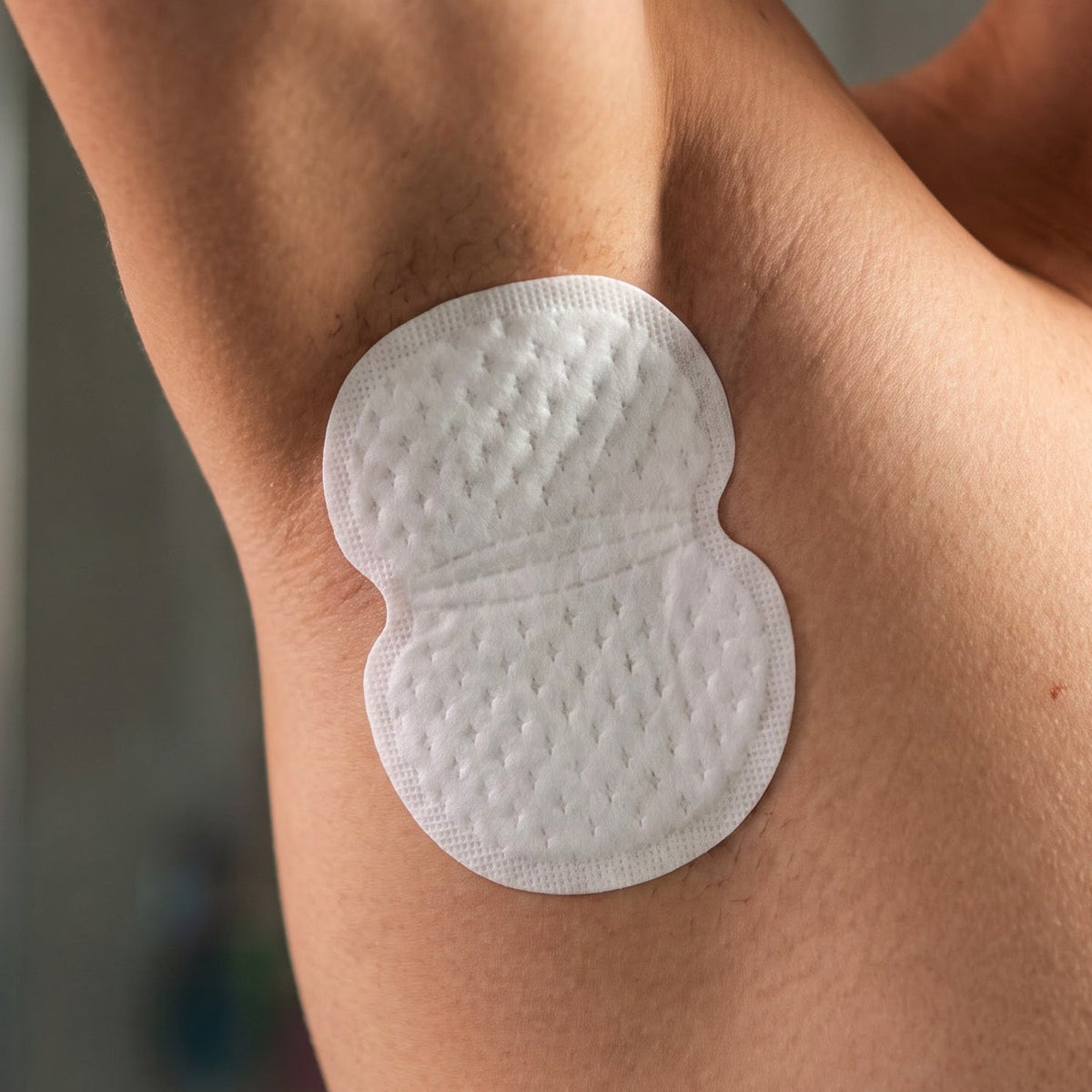 A white, textured sweat pad is shown adhered to a person's bare armpit, with light stubble visible.