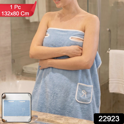 Woman wearing a light blue wearable bath towel with a white trim and a small pocket, with product dimensions overlay.