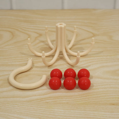 The disassembled cream multi-hook hanger parts, including the S-hook, base, and six red balls, are laid out on a light