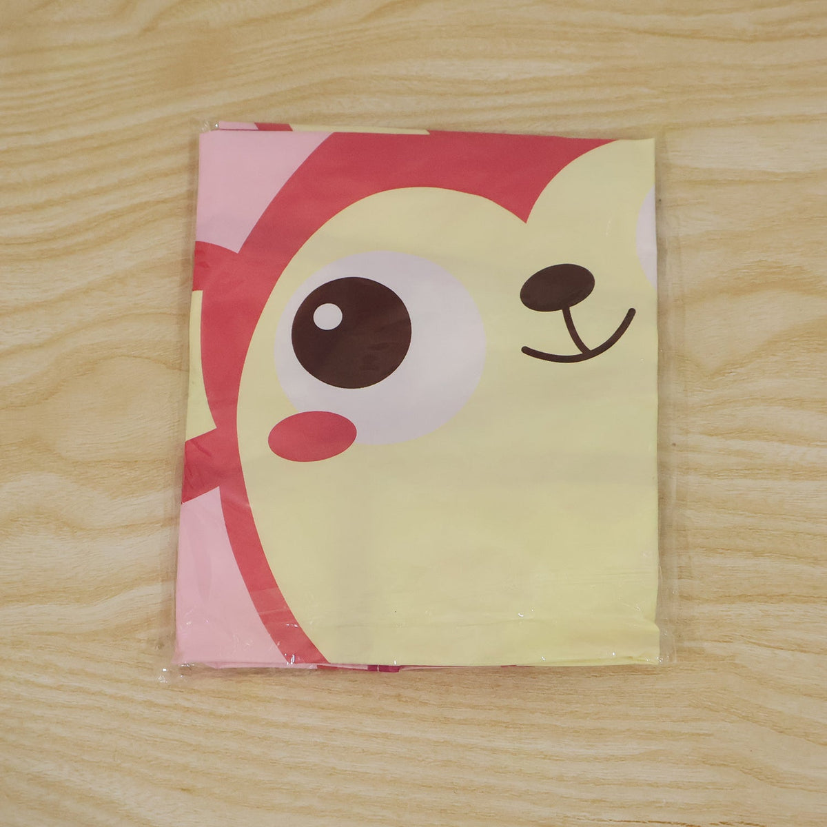 A clear plastic-wrapped, folded pink apron with a partial monkey face print is on a light wooden surface.