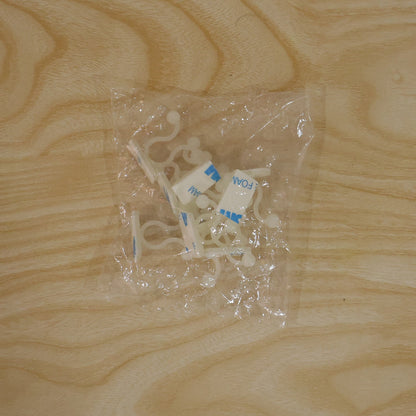 Several white plastic self-adhesive plant clips are visible inside a clear plastic bag on a light wooden surface.
