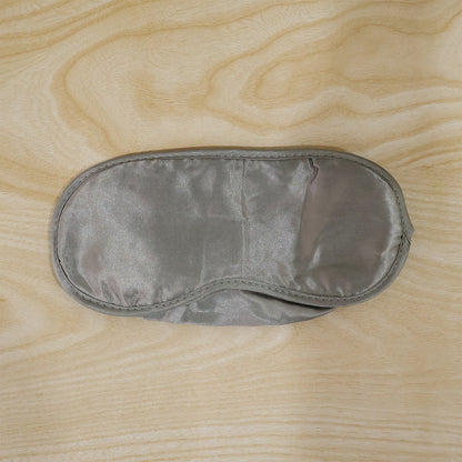 A grey satin sleeping eye mask with a smooth surface is laid flat on a light wooden background.