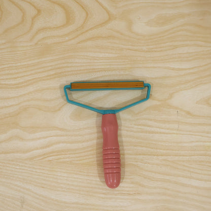 Pink and blue lint remover with textured handle for removing pet hair and lint from fabric.