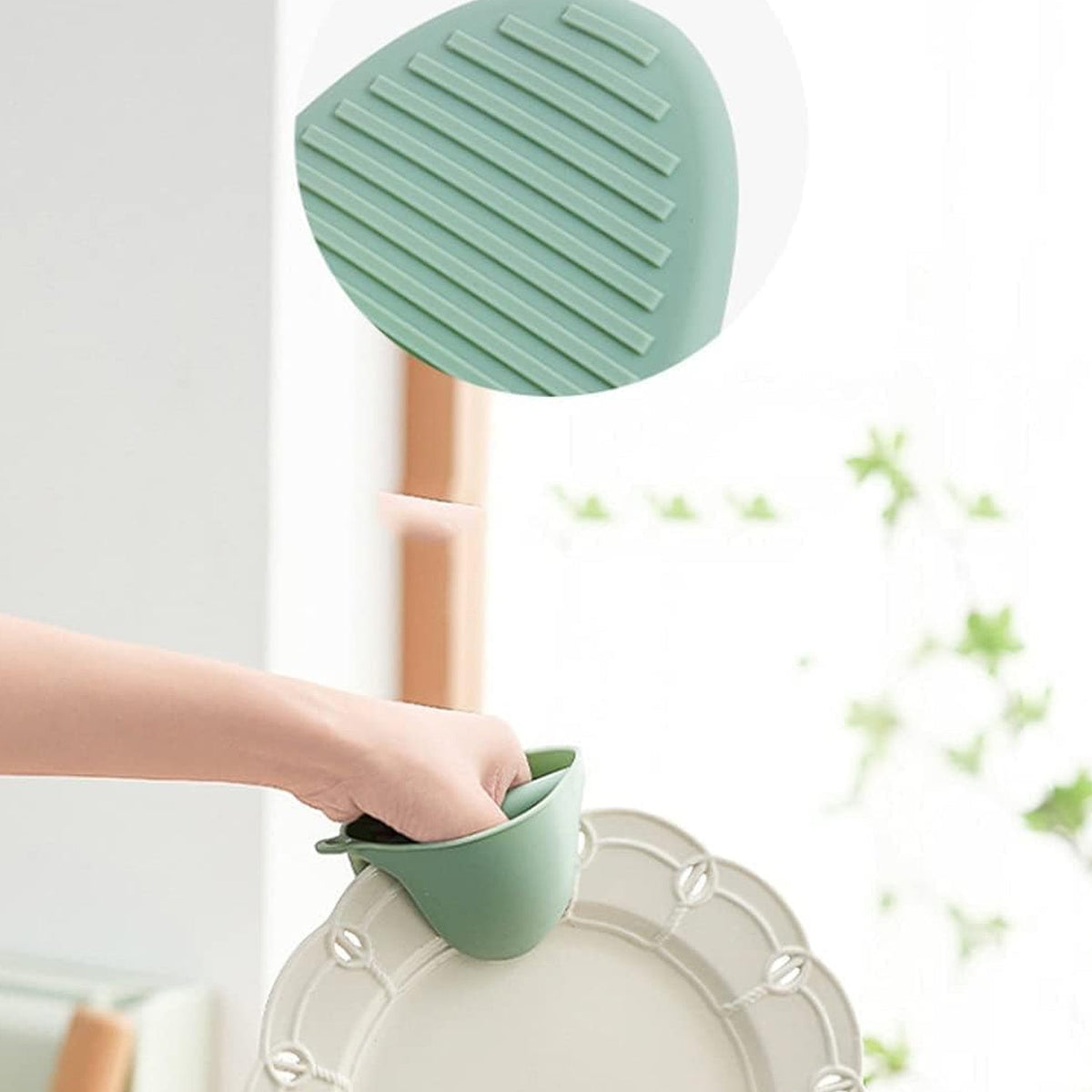 A hand uses a green silicone mini oven mitt to hold a white decorative plate.