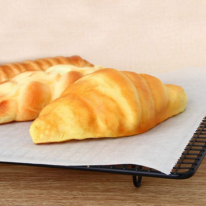 A golden-brown croissant and another pastry on a sheet of white baking paper on a black wire rack.