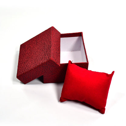 An open red textured gift box with its lid ajar, and a red velvet pillow placed next to it on a white background.