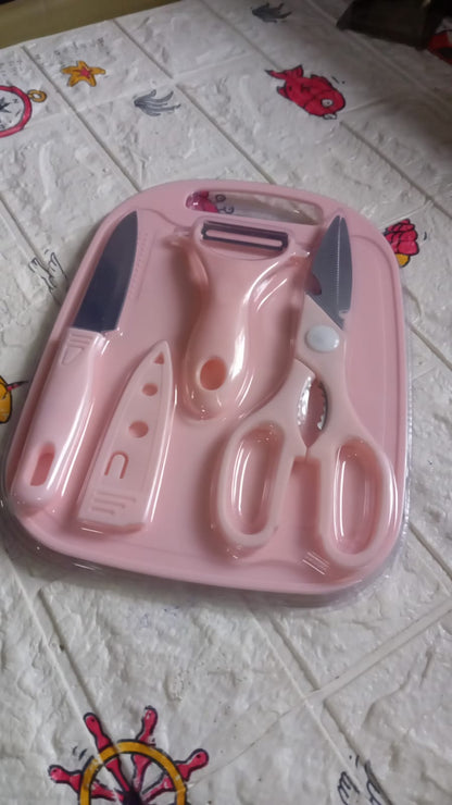 The pink cutting board set, including a knife, peeler, and scissors, is sealed in clear plastic packaging on a patterned