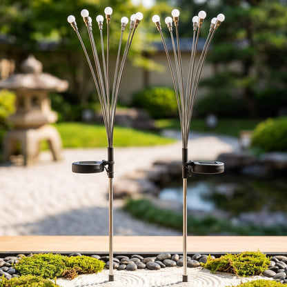 Two solar firefly lights with silver stems and white bulbs stand in a Japanese-style garden with raked gravel.