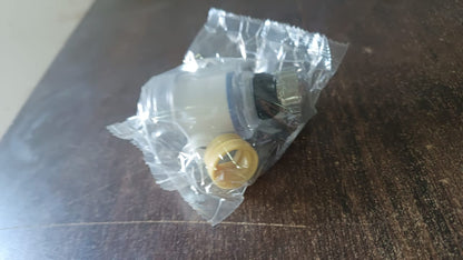 The clear plastic faucet aerator with a yellow base, sealed in a clear plastic bag on a dark wooden surface.