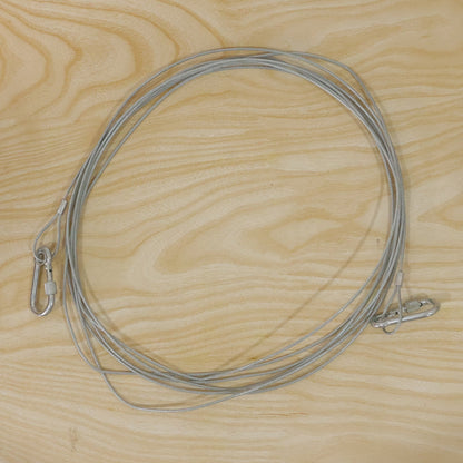 A long, silver stainless steel wire rope with two carabiner hooks is laid out on a light wooden surface.
