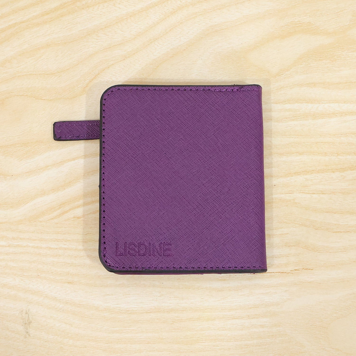 A closed purple bifold wallet with the brand name "LISDINE" embossed on the front, resting on a light wooden surface.