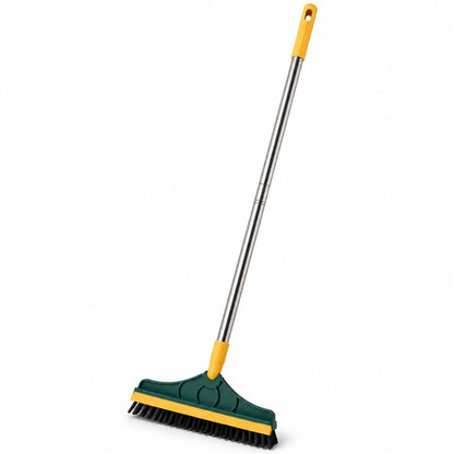 A green and yellow floor cleaning brush with a long metal handle is angled on a white background, showcasing its design.