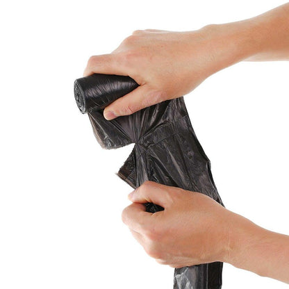 Two hands unroll a black garbage bag from a roll, tearing it along a perforated line.