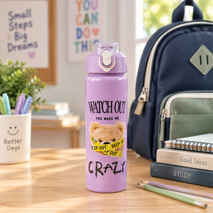 A medium-sized purple water bottle with a teddy bear design on a desk with school supplies and a backpack in the background.