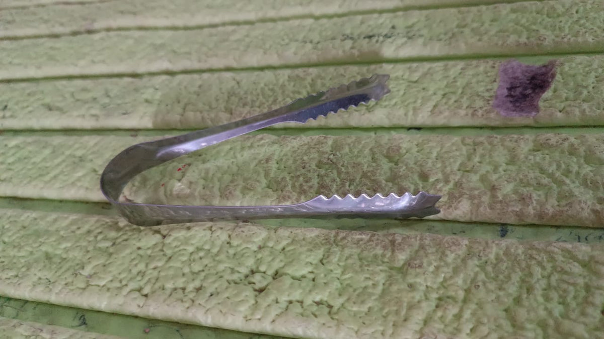 A silver tong rests on a textured light green surface with horizontal ridges.