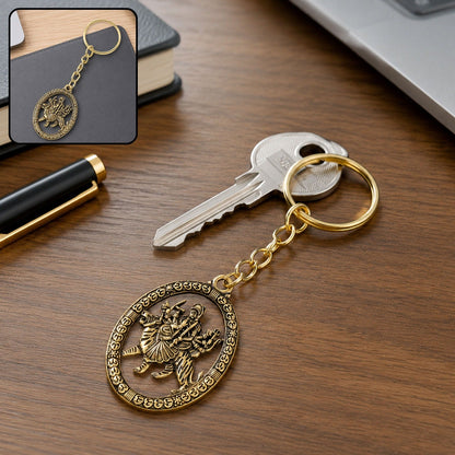 A golden keychain with an oval pendant depicting a deity, resting on a wooden desk next to a silver key.